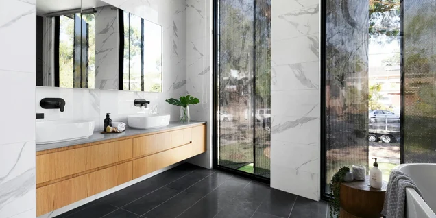Modern bathroom with double vanity, marble walls, and large windows by Timberline Build Co.