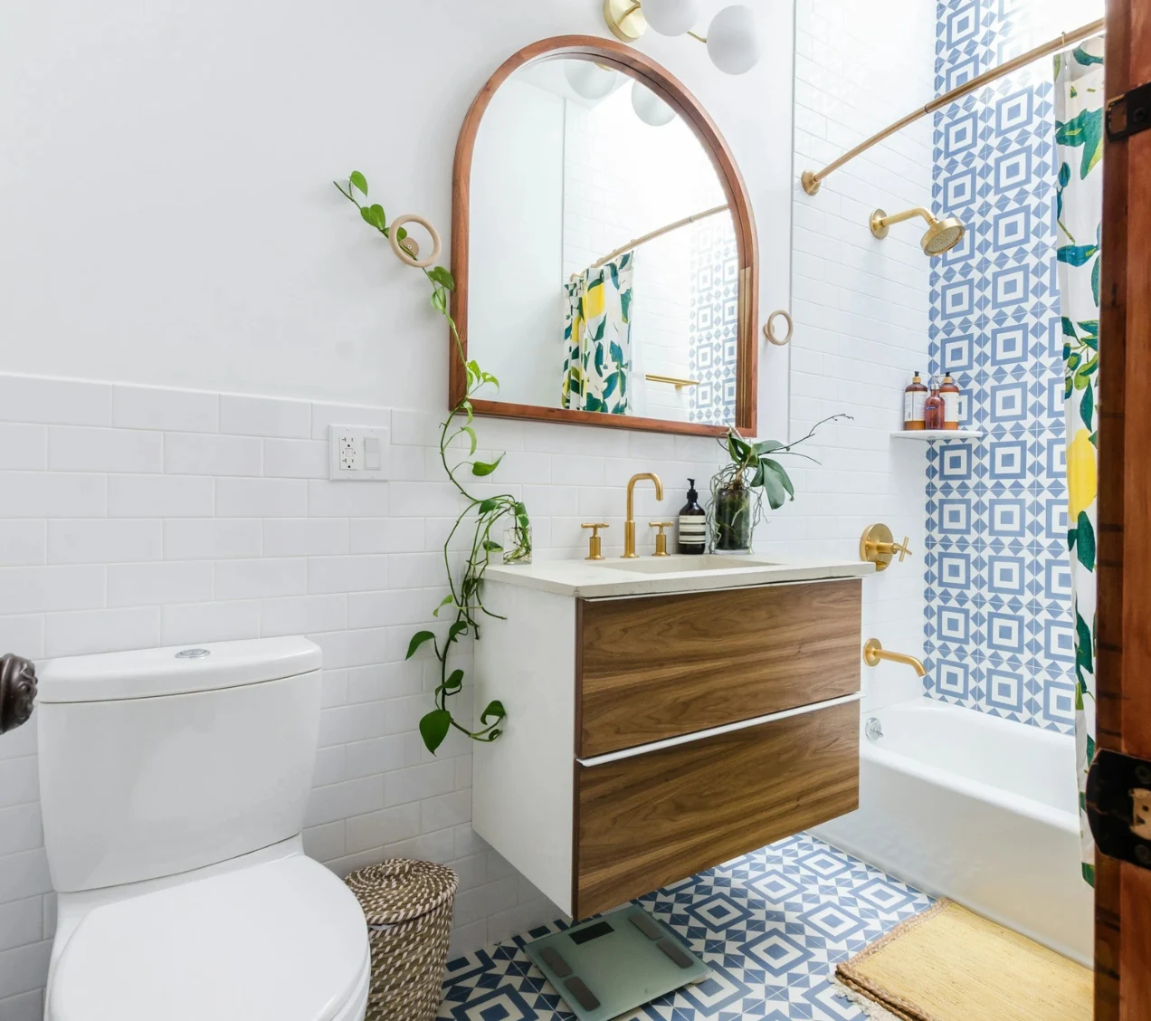Stylish bathroom remodel with blue tile floor, wood vanity, and arched mirror.
