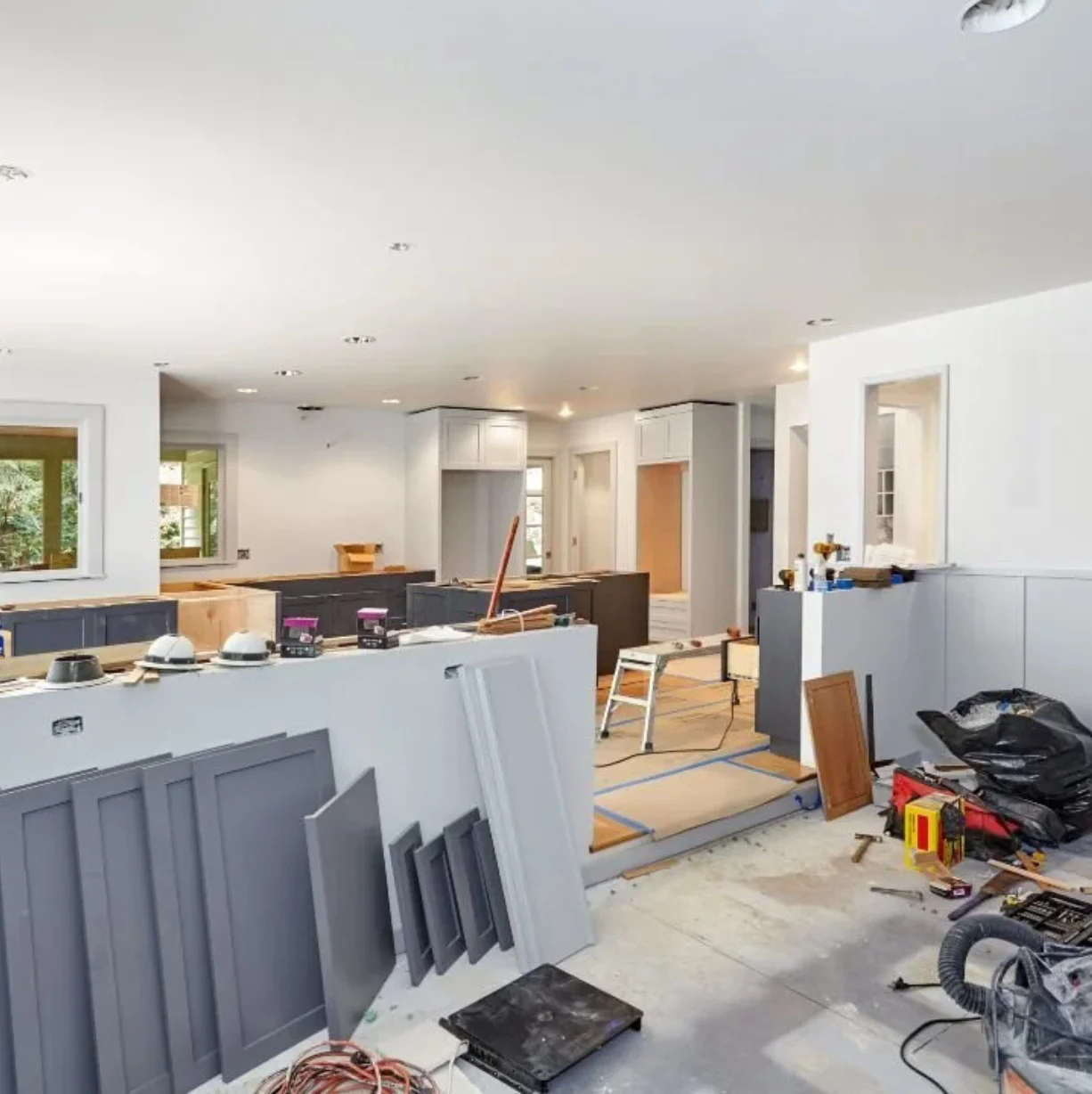 Kitchen renovation in progress: gray cabinets, tools, and construction materials in a bright, spacious room.