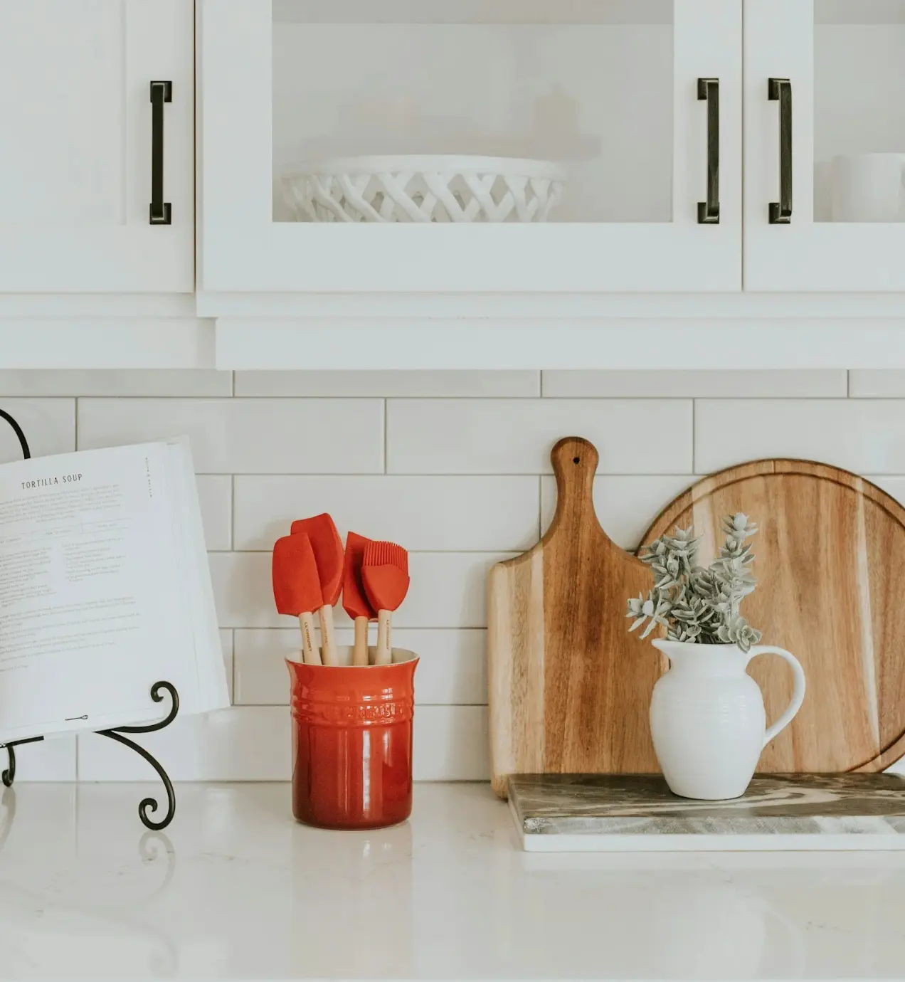 White kitchen countertop with red utensils, cutting boards, and a Tortilla Soup recipe book.