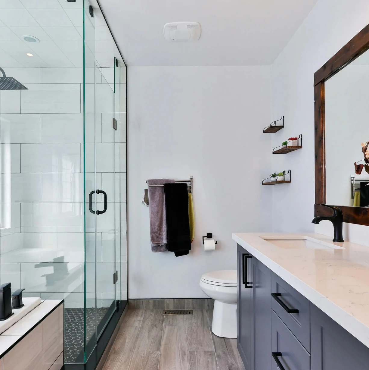 Modern bathroom with glass shower, gray vanity, wood-framed mirror, and white walls.