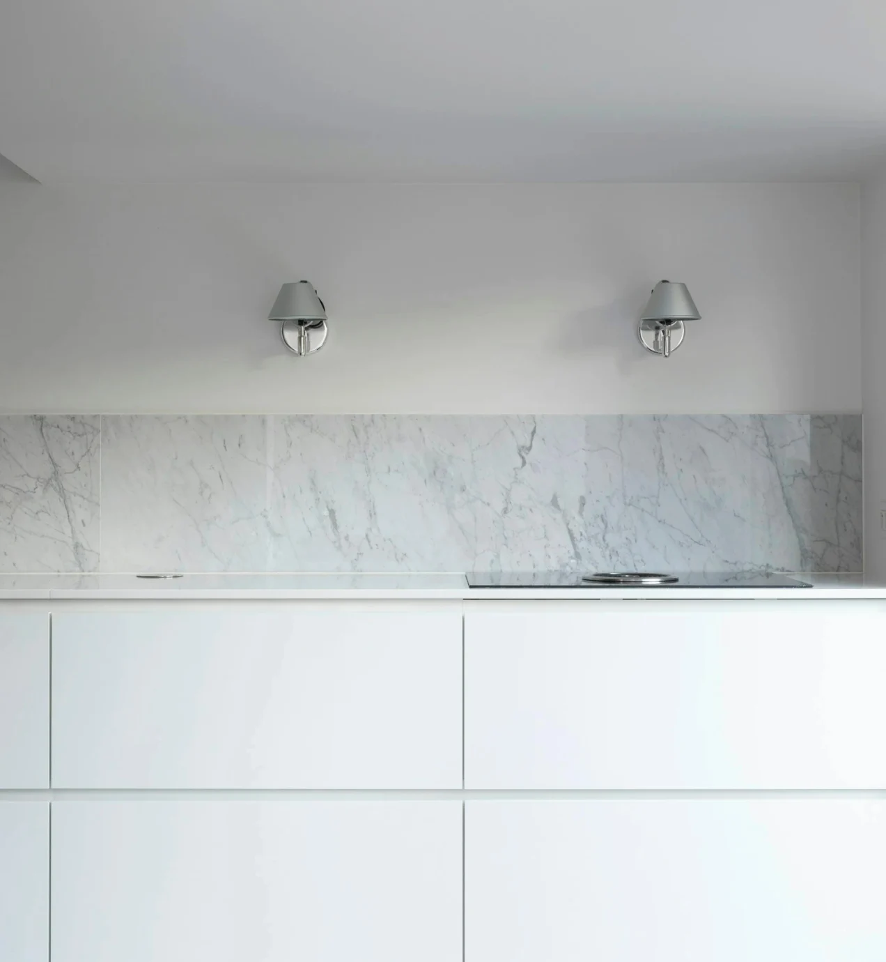 Sleek white kitchen cabinets with marble backsplash and modern sconces. Dana Point kitchen remodel.