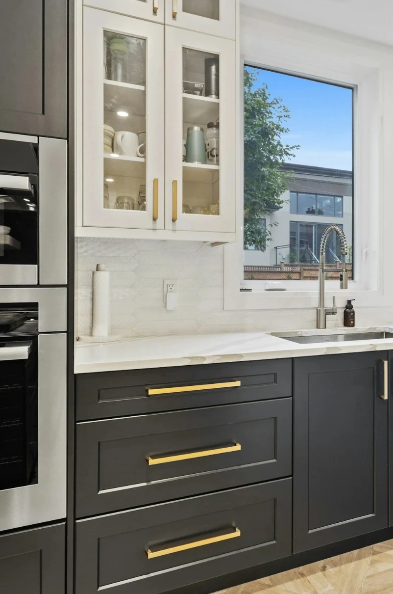 San Clemente kitchen remodel with black cabinets, gold hardware, and white countertops near a window.