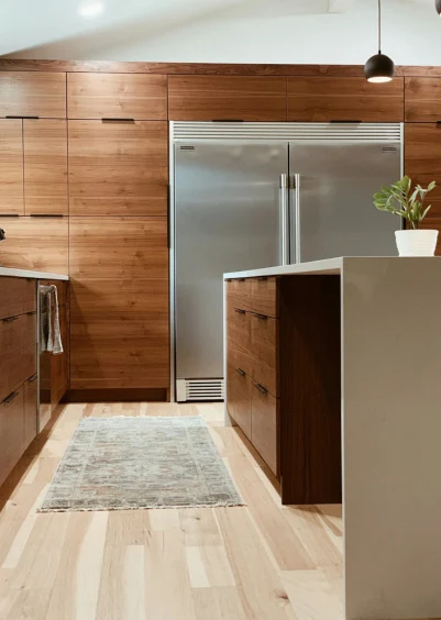 Modern kitchen with wood cabinets, stainless steel refrigerator, and a light wood floor.