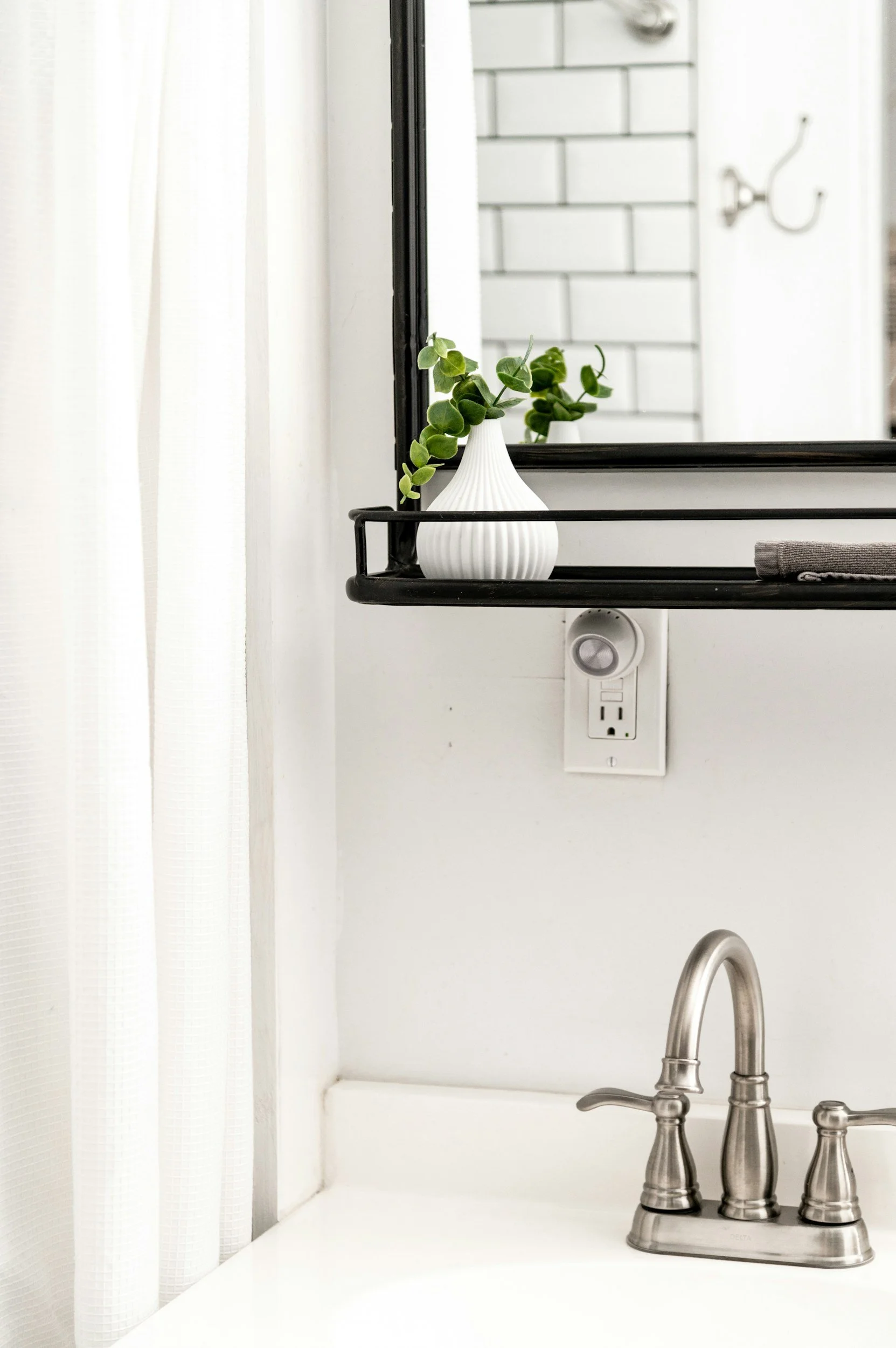Bathroom detail: sink, mirror, greenery, outlet. Clean, modern design.