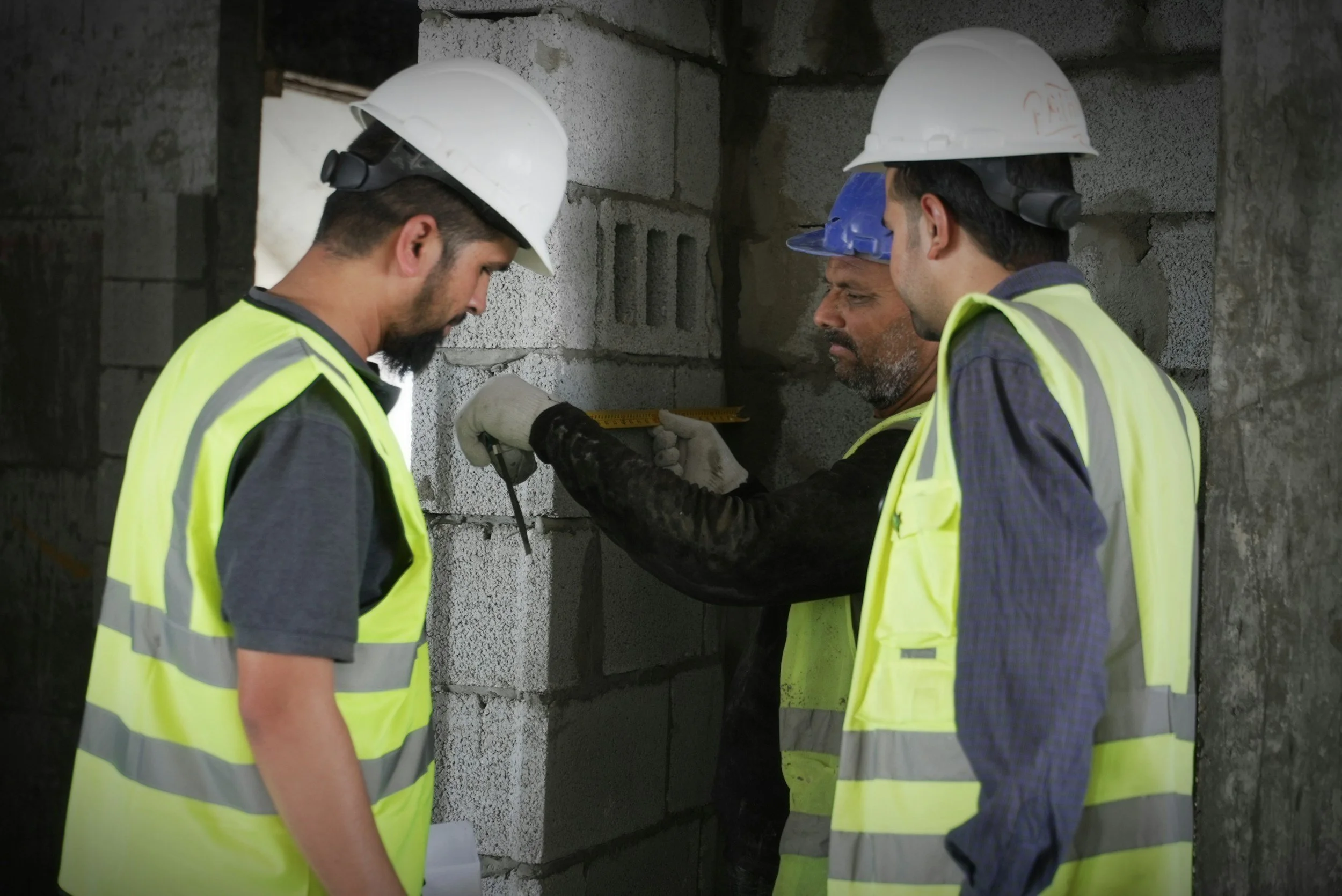 Comprehensive Guide to General Contracting: Local Services, Costs, & Hiring Tips 2 Construction workers in hard hats inspecting brickwork with a measuring tape. General contracting.