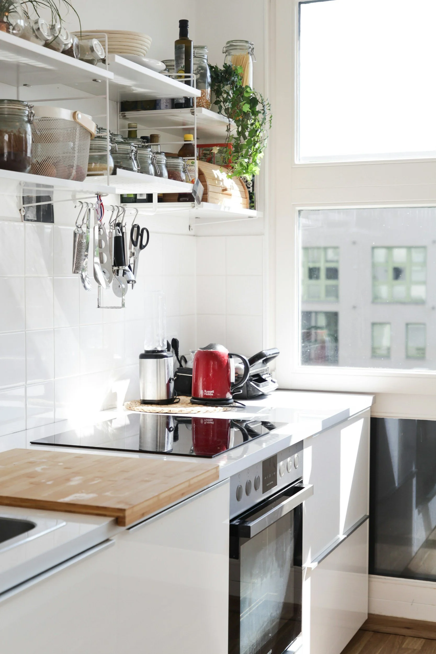 Bright, modern white kitchen with open shelving, countertop appliances, and a built-in oven.