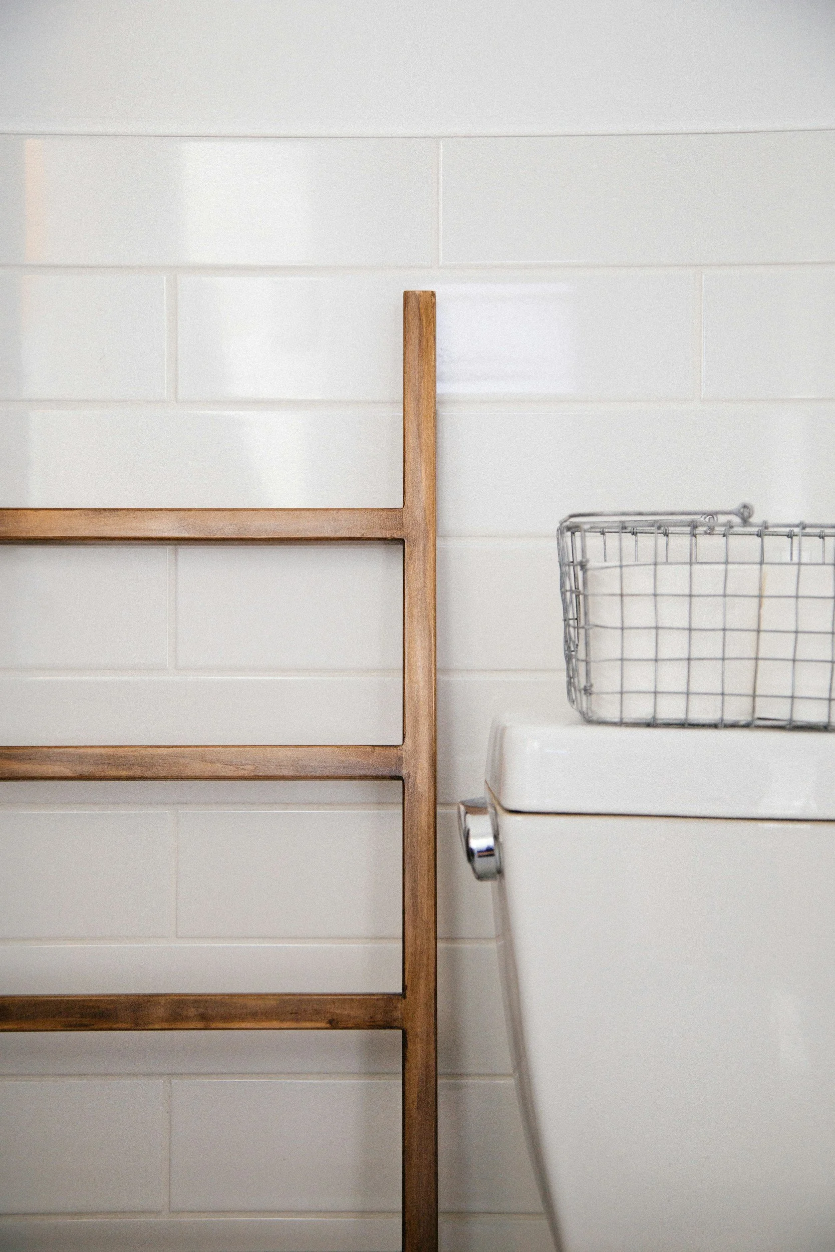 Bathroom: Wooden ladder, toilet with wire basket, white tile wall.