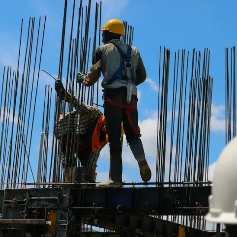 Construction workers building a structure with rebar, wearing hard hats and safety harnesses.