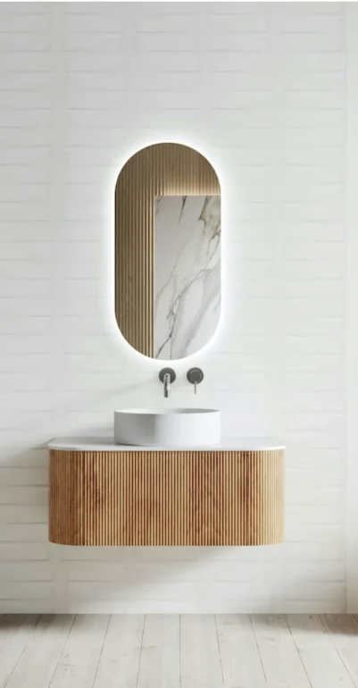 Modern bathroom renovation with wood vanity, vessel sink, and oval lighted mirror. High-end bathroom design.
