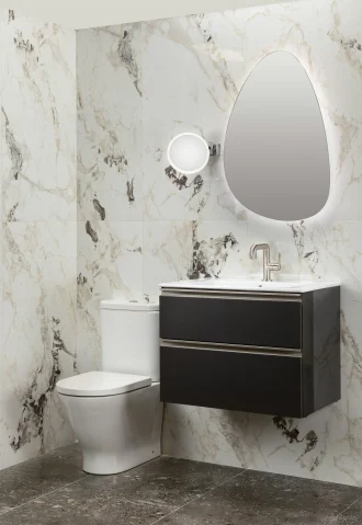 Modern bathroom remodel in Ladera Ranch with marble walls, dark vanity, oval mirror, and white toilet.
