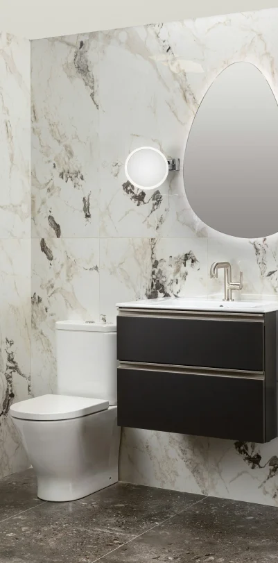 Modern bathroom remodel in Ladera Ranch with marble walls, dark vanity, oval mirror, and white toilet.