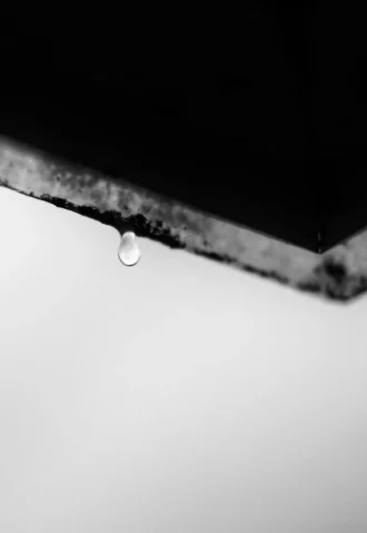 Water droplet hanging from a dark, weathered edge. Possible water damage situation.